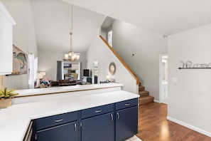 A spacious kitchen with a large island, dark blue cabinets, and a white countertop. A wooden staircase leads to an upper level. - The Joyful Getaway For 8! (Branson)