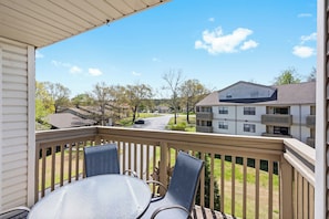 A balcony with a table and chairs, overlooking a residential area with houses and a road. - The Joyful Getaway For 8! (Branson)