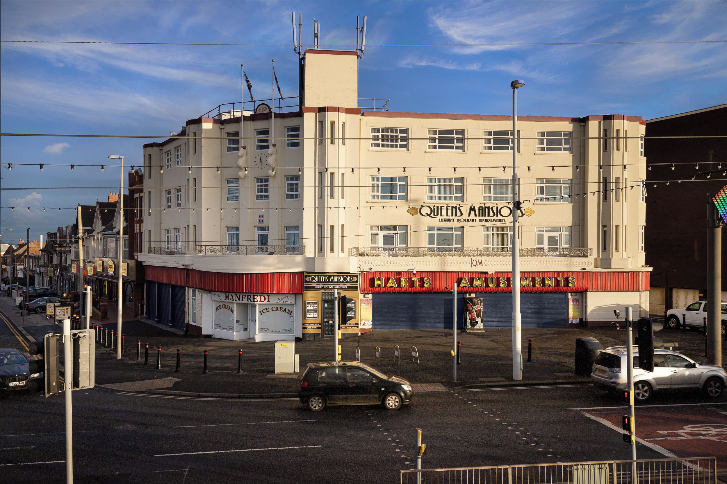 A multi-story building with a sign for 'Queens Mansion' and 'Harts Appliances'.