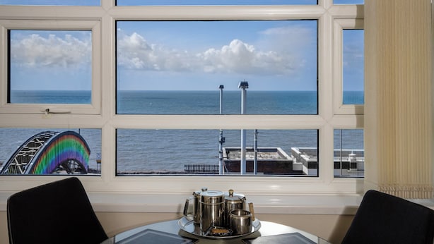Un espace repas avec une table et des chaises, une vue sur la mer à travers de grandes fenêtres et une grande roue en arrière-plan.