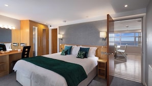 Une chambre d’hôtel moderne dotée d’un grand lit, d’un bureau avec un ordinateur et offrant une vue sur la mer grâce à une grande fenêtre.