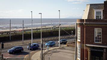 A coastal street with a view of the sea, a building with a sign 'The Powder Room', and parked cars.