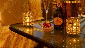 Une table dressée avec des coupes à champagne, une bouteille et un dessert, sur un balcon offrant une vue sur le coucher de soleil.