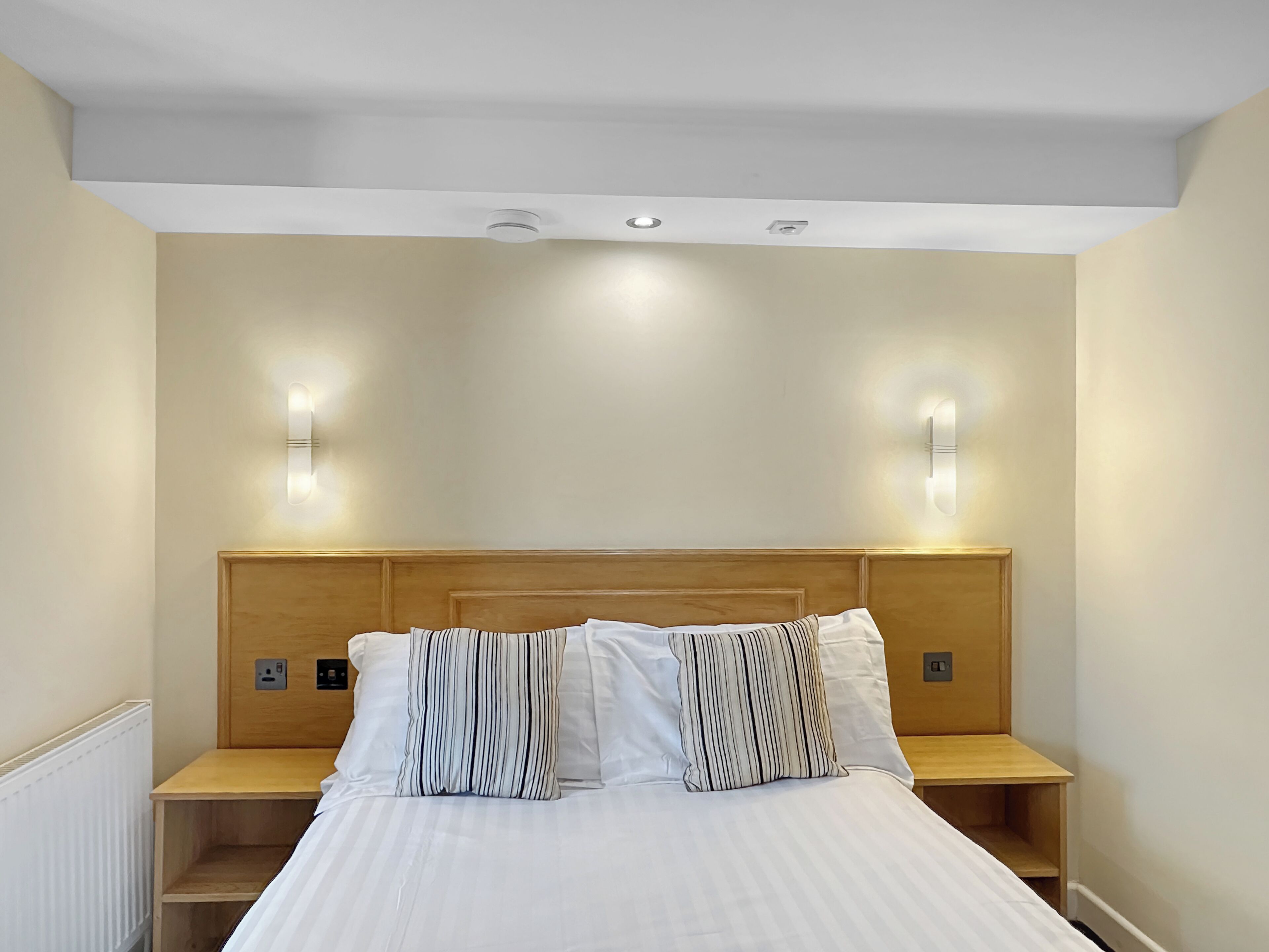 A hotel room with a wooden headboard, two bedside tables, and a bed with striped pillows.
