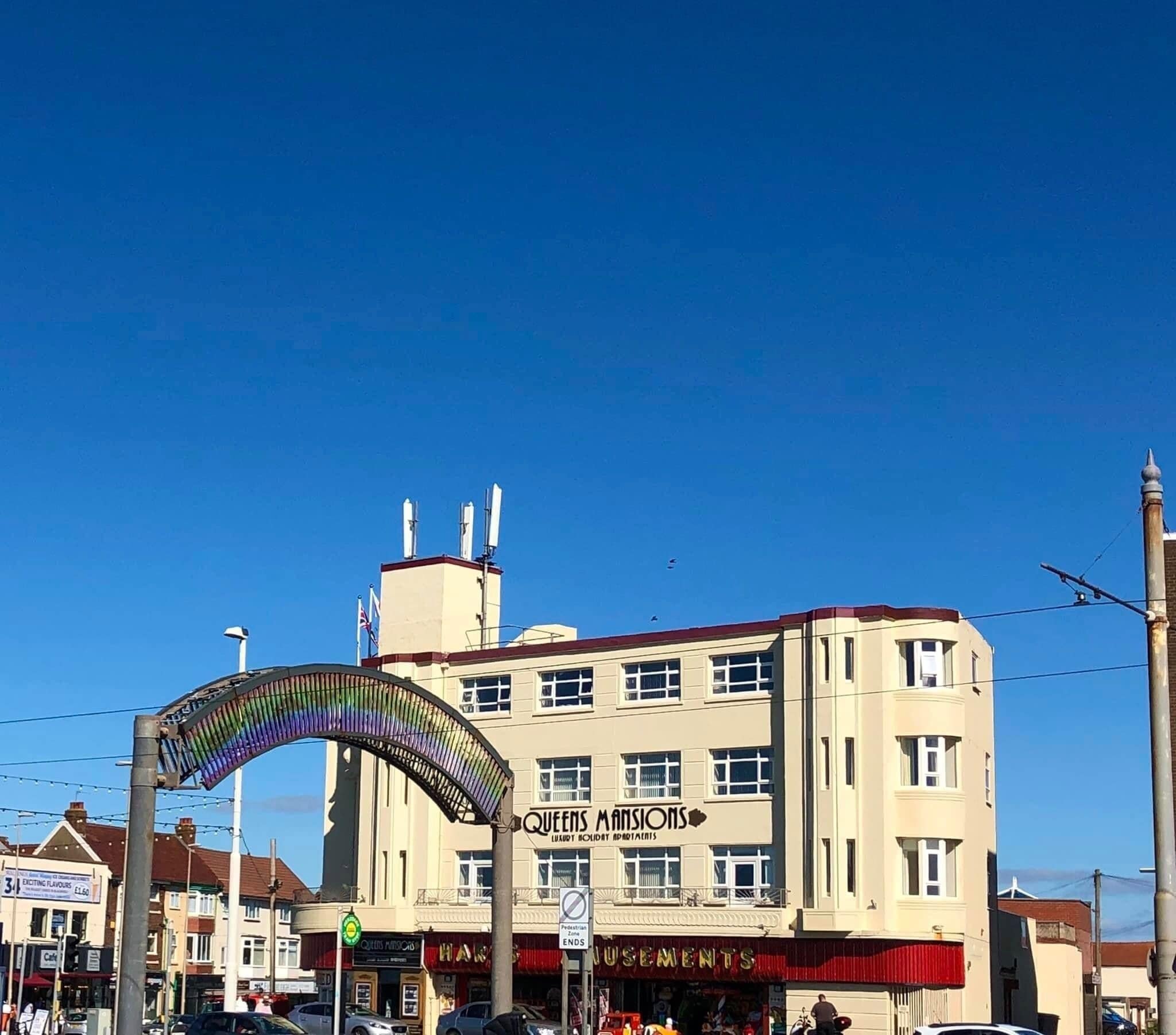 A building with a sign reading "Queens Mansions" and a pedestrian archway.