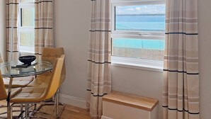 Une pièce comprenant une table à manger, des chaises, une vue sur la mer et des rideaux.