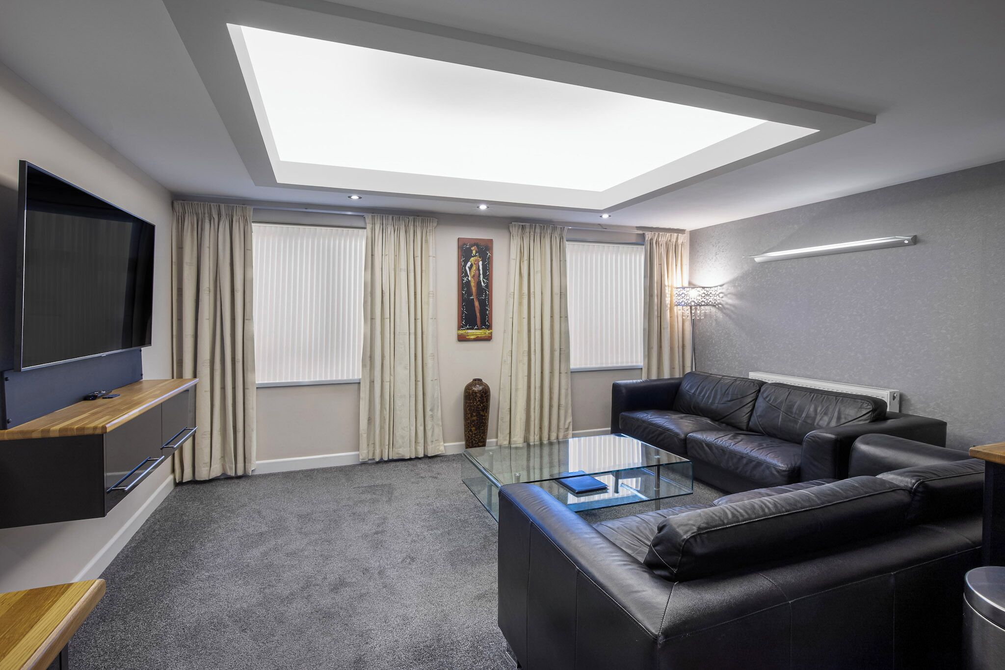 A modern living room with a flat-screen TV, leather sofa, glass coffee table, and a skylight.