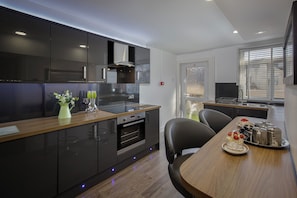 Una cocina moderna con armarios oscuros, horno empotrado y comedor con mesa y sillas de madera.