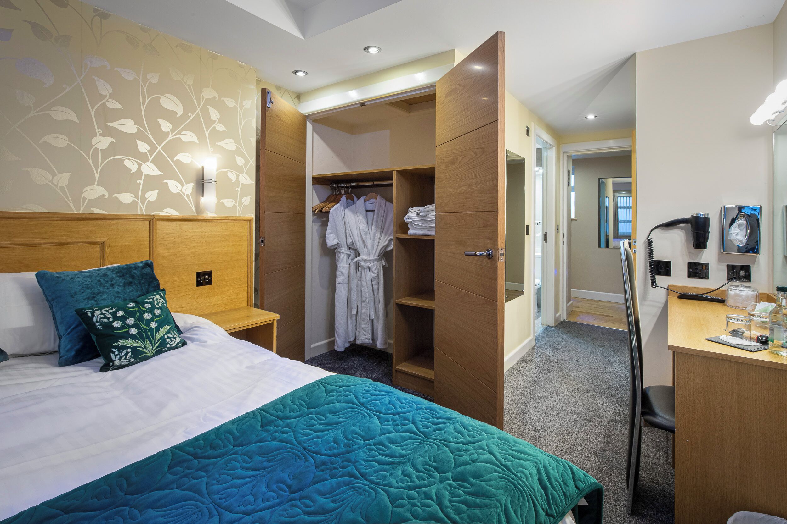 A hotel room with a bed, a desk, a wardrobe, and a bathroom.