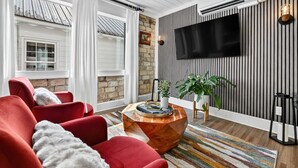 A modern living room with red sofas, a wooden coffee table, a striped rug, a TV mounted on a striped wall, and a brick wall. - Luxury Suite in the heart of downtown Blue Ridge (Blue Ridge)