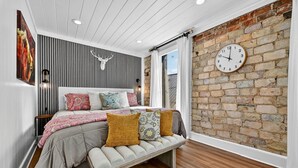A bedroom with a bed, bench, wooden floor, brick wall, and a clock. - Luxury Suite in the heart of downtown Blue Ridge (Blue Ridge)
