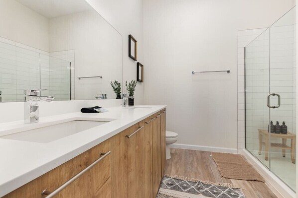 A modern bathroom with a white vanity, a glass shower enclosure, and a wooden floor.