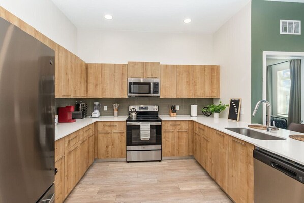 Una cocina moderna con armarios de madera, electrodomésticos de acero inoxidable y encimera blanca.