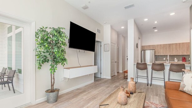 Una sala de estar moderna con televisor de pantalla plana, un comedor con mesa de madera y una cocina con taburetes de bar.