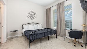 Un dormitorio con una cama, un escritorio, una silla, una mesita pequeña y una obra de arte en la pared.