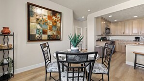 A modern kitchen with wooden cabinets, a central island, and a dining area with a glass table and metal chairs. - Par Paradise by Mesquite Vacation Rentals with Views of the Fairways and $510 in free daily activities (Mesquite)
