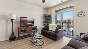 A living room with a television, a coffee table, a sofa, and a large window with a view of a building. - Par Paradise by Mesquite Vacation Rentals with Views of the Fairways and $510 in free daily activities (Mesquite)