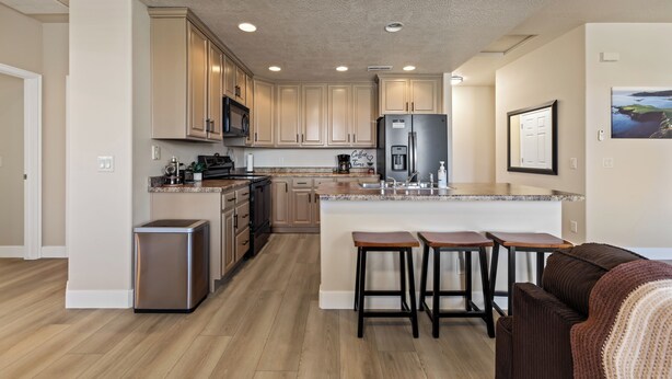 A modern kitchen with wooden cabinets, a stainless steel refrigerator, and a bar area with stools. - Par Paradise by Mesquite Vacation Rentals with Views of the Fairways and $510 in free daily activities (Mesquite)