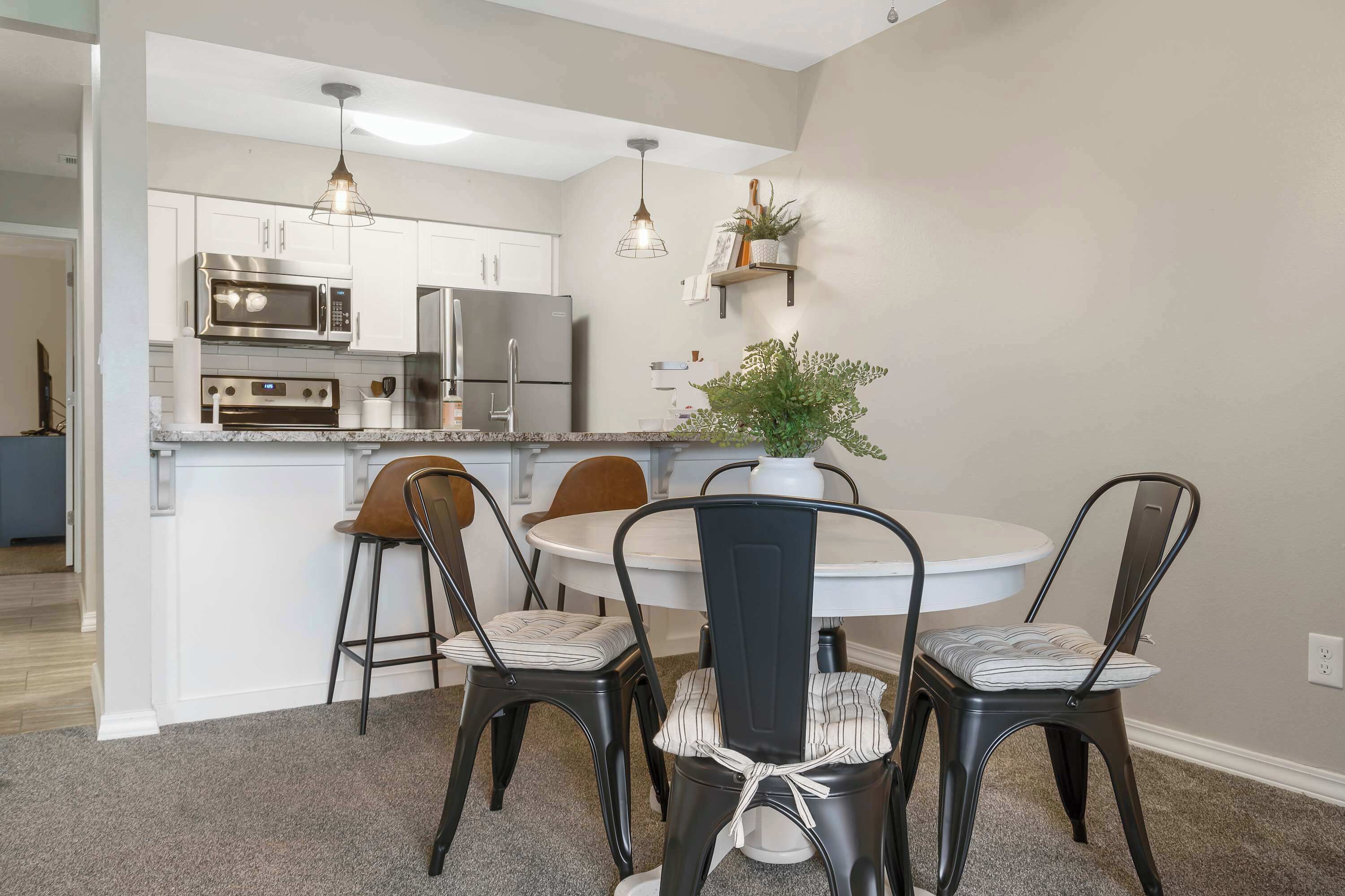 A modern kitchen with white cabinets, stainless steel appliances, and a dining area with a round table and four chairs.