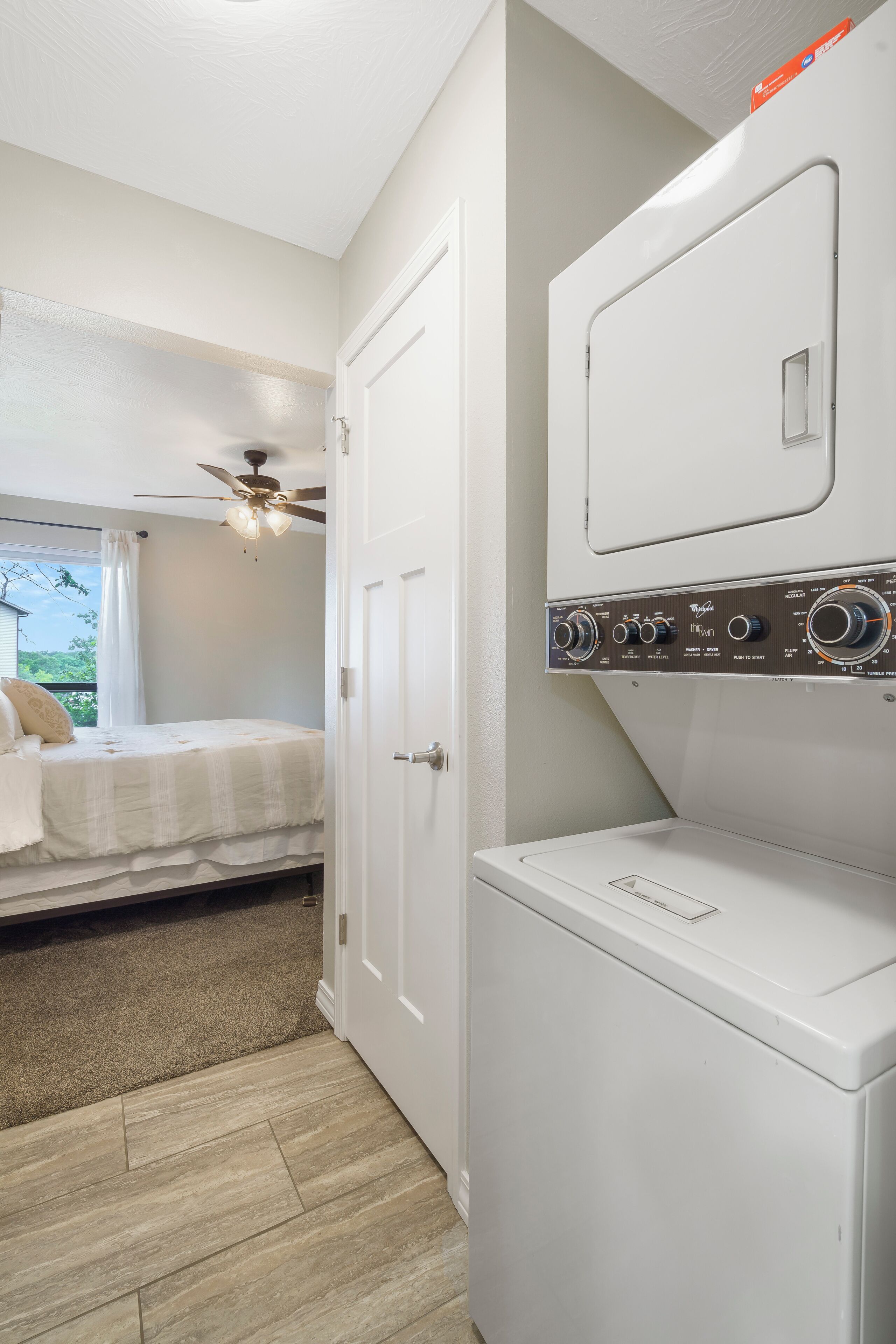 Une buanderie équipée d’un lave-linge et d’un sèche-linge, une chambre avec un ventilateur de plafond et une vue sur la verdure environnante.