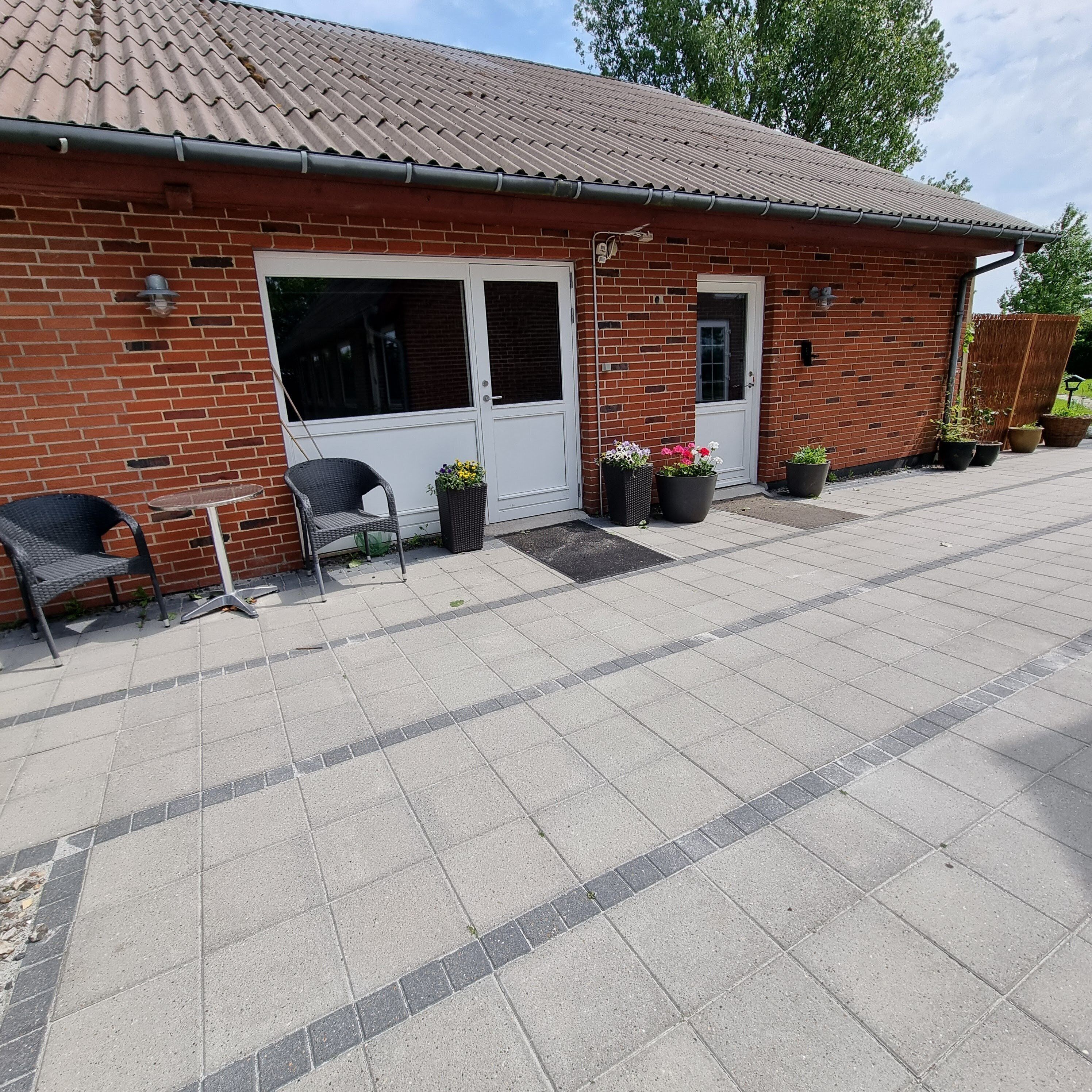 A brick building with a tiled roof, a front door, and a small patio area with a chair and potted plants.