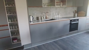 A modern kitchen with a built-in oven, a dishwasher, and a large cabinet with glassware.