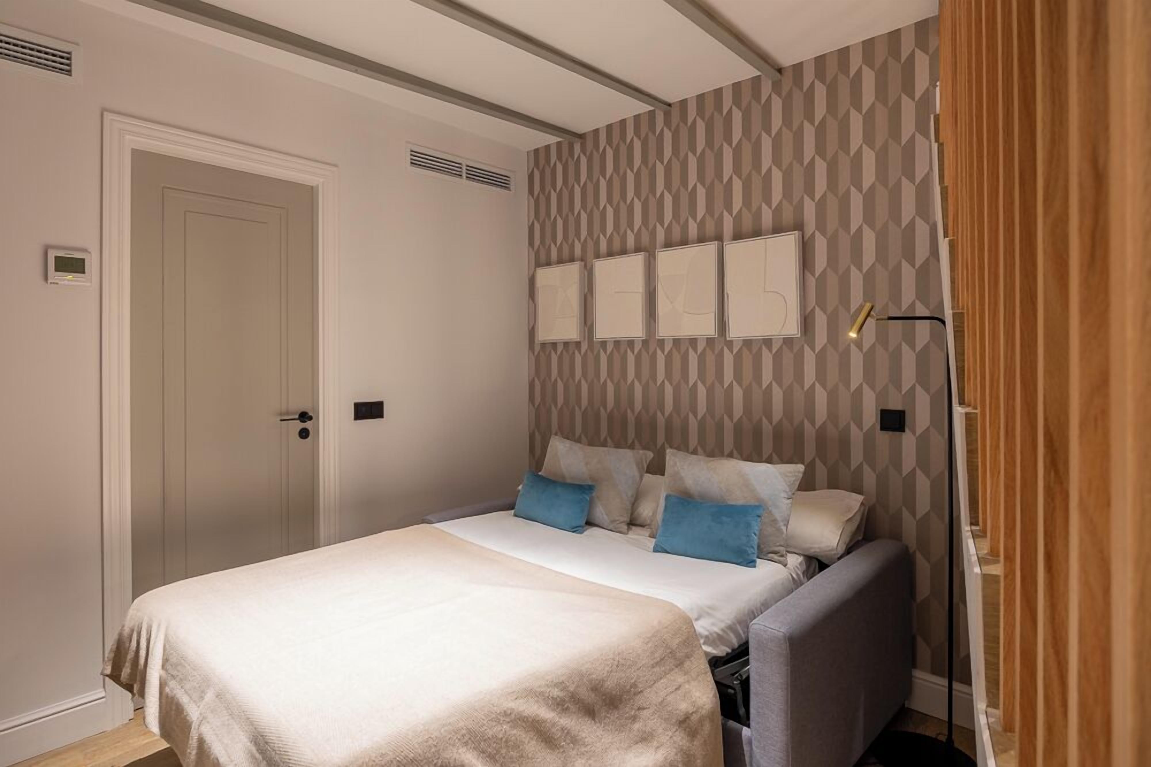 Een slaapkamer met een bed, hoofdeinde, een aan de muur bevestigde televisie en een deur.
