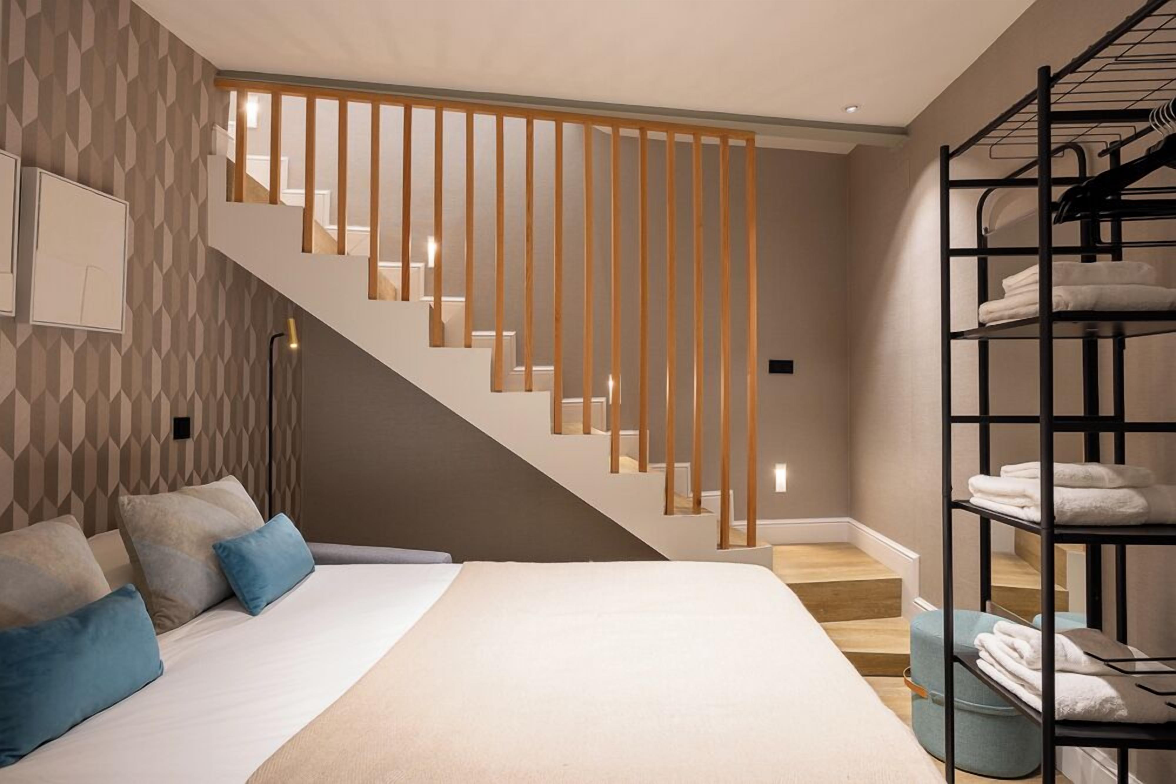 A modern hotel room with a large bed, a wooden staircase, and a black metal shelf with towels.