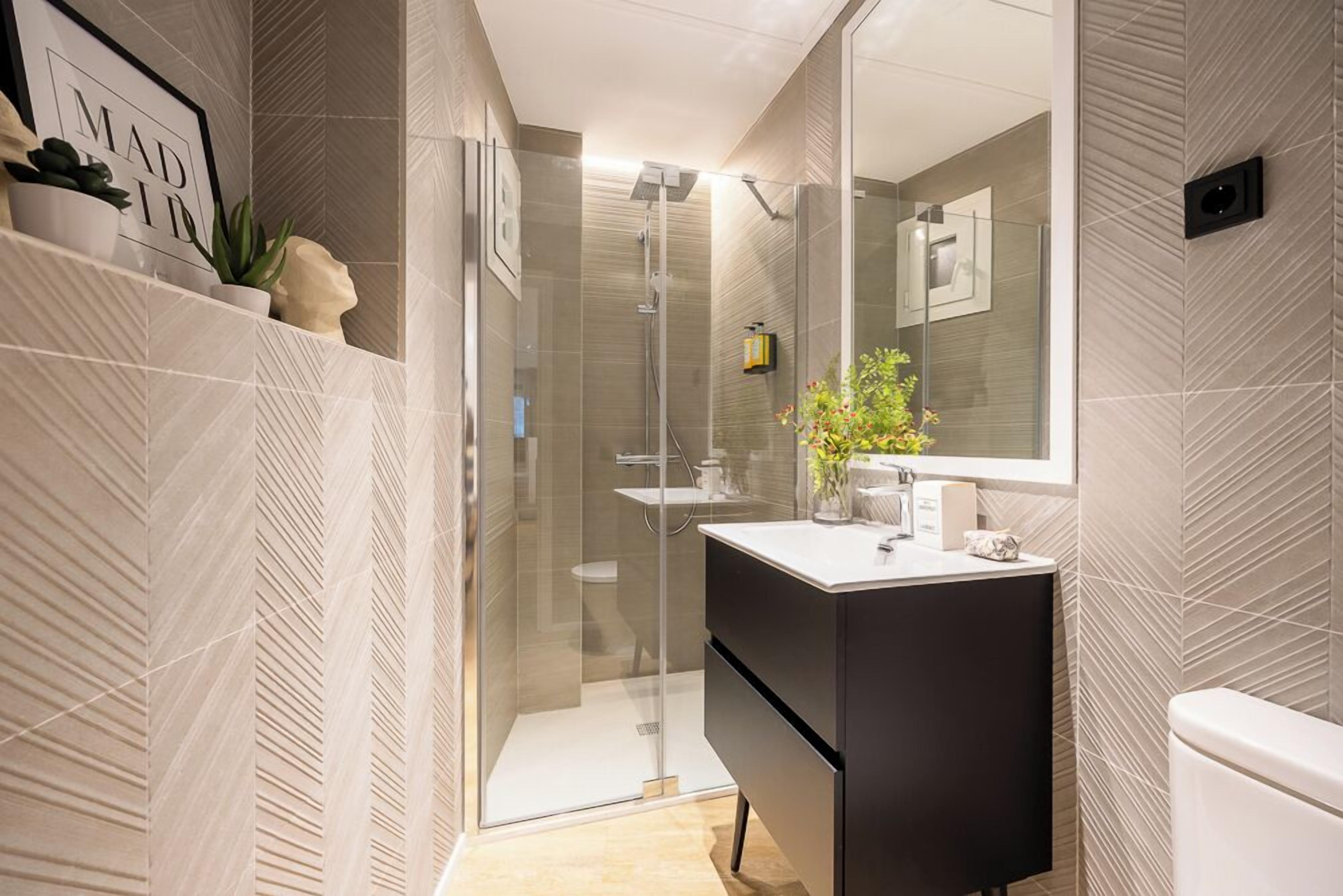 A modern bathroom with a glass-enclosed shower, a black vanity, and a large mirror.