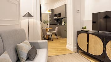 A modern living room with a grey sofa, a black TV stand, and a dining area with a table and chairs.