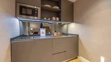Una kitchenette compacta con microondas, horno y un estante con vajilla.