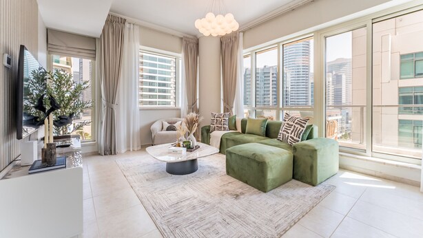 Een moderne woonkamer met een groene modulaire bank, een ronde salontafel en een groot raam met uitzicht op de stad.