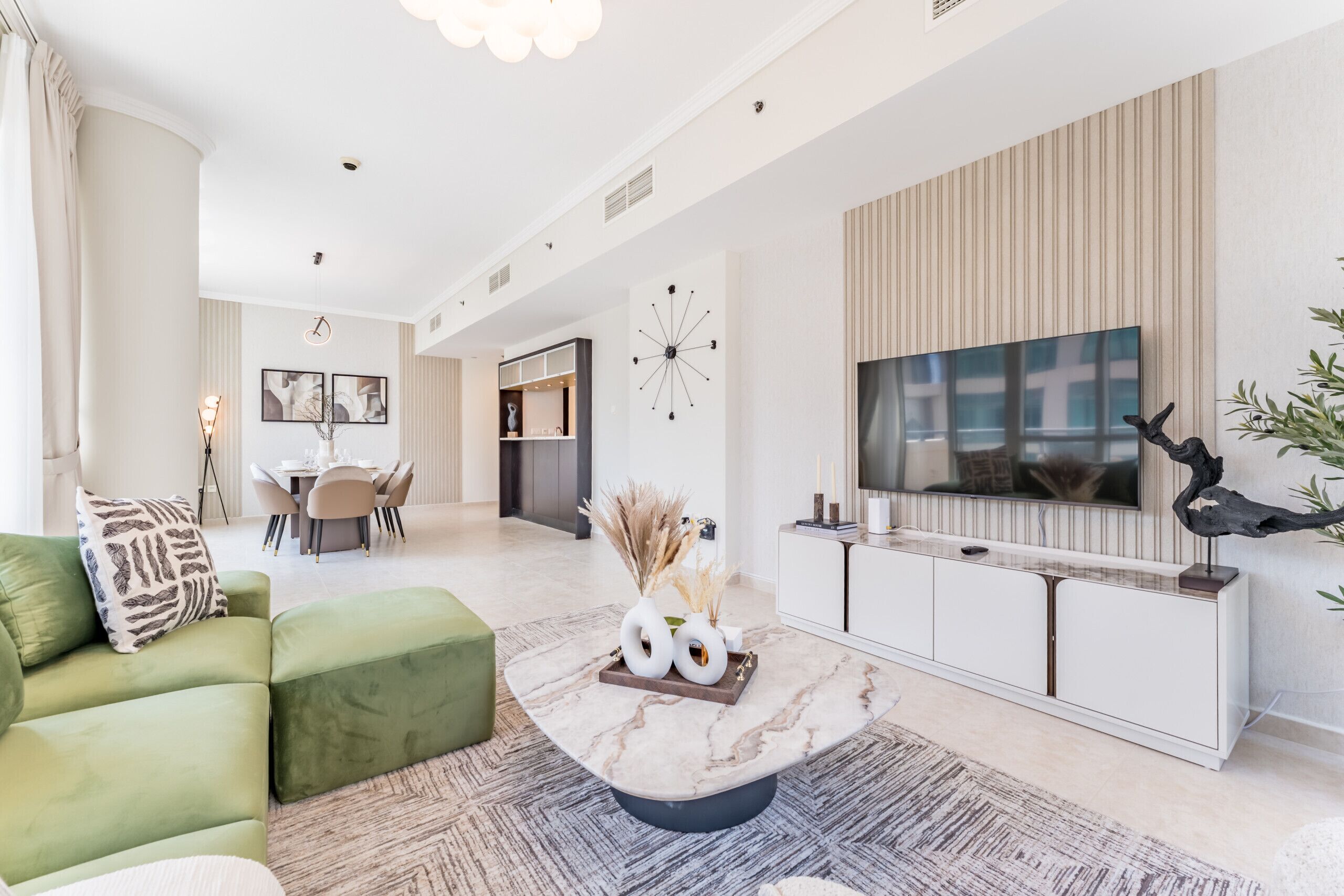 Una sala de estar moderna con un sofá verde, una mesa de centro de mármol y un televisor sobre un mueble blanco.