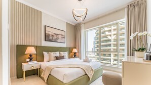 Een moderne hotelkamer met een groot bed, twee nachtkastjes met lampen, een groen hoofdeinde, een groot raam met uitzicht op de stad, en een klein bureau met een plant.