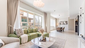 Een moderne woonkamer met een groene bank, een marmeren salontafel en een eethoek op de achtergrond.