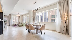 Een ruime woonkamer met een eethoek, grote ramen en een moderne kroonluchter.
