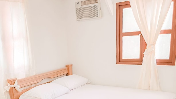 A neatly made bed with white linens, a wooden headboard, and a window with curtains. - Hotel Villa Santa Maria  (Santa Fe de Antioquia)