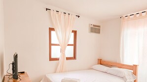 A neatly arranged bedroom with a wooden bed, a bedside table with a television, a window with curtains, and a ceiling light. - Hotel Villa Santa Maria  (Santa Fe de Antioquia)
