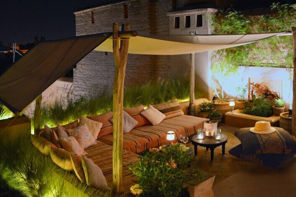 A cozy outdoor seating area with a cushioned sofa, a small table with candles, and various potted plants.