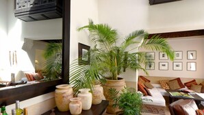 A living room with a sofa, a coffee table, a large mirror, and several potted plants. - Riad Douceur (Marrakech)