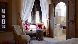 A cozy room with a bed, a chair, a small table with a vase of flowers, and a window with curtains. - Riad Douceur (Marrakech)
