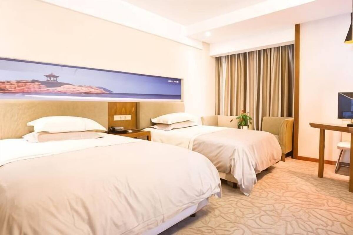 A hotel room with two beds, a desk, a TV, and a large window with curtains.