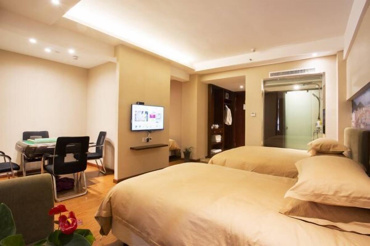 A hotel room with two beds, a desk with a computer, a TV, and a bathroom with a mirror and shower.