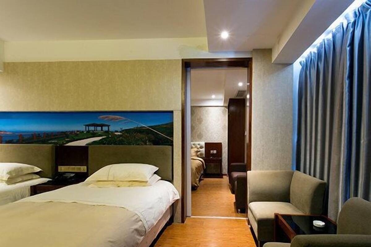 A hotel room with two beds, a sofa, a painting of a landscape, and a view of a building through the window.