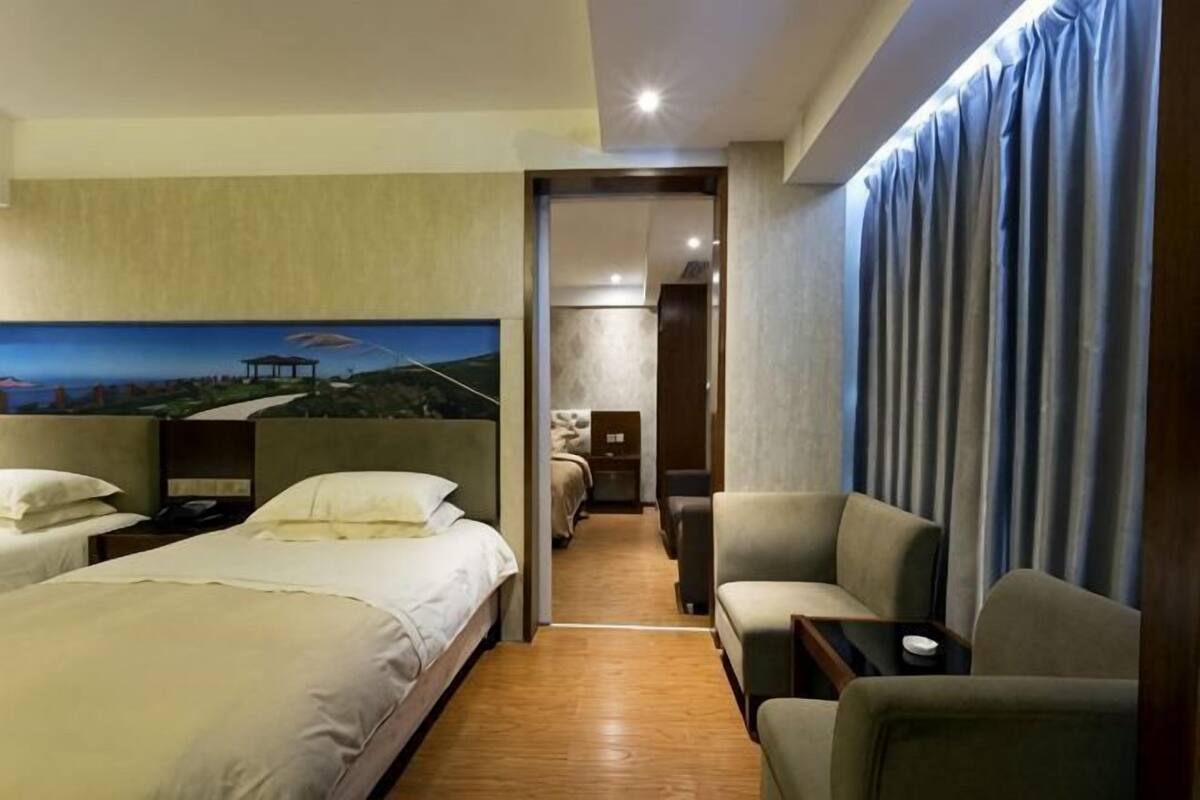 A hotel room with a bed, two chairs, a small table, and a painting on the wall.