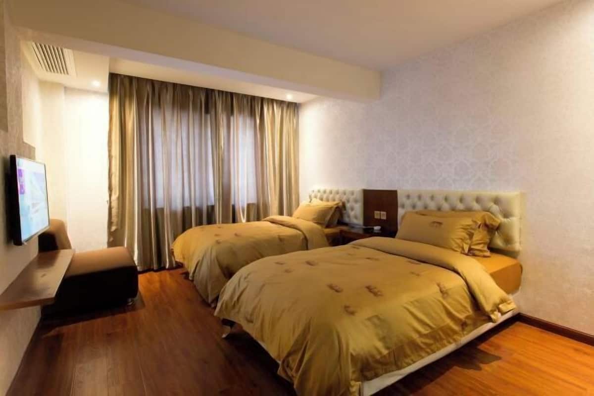 A hotel room with two beds, a TV, a sofa, and a large window with curtains.