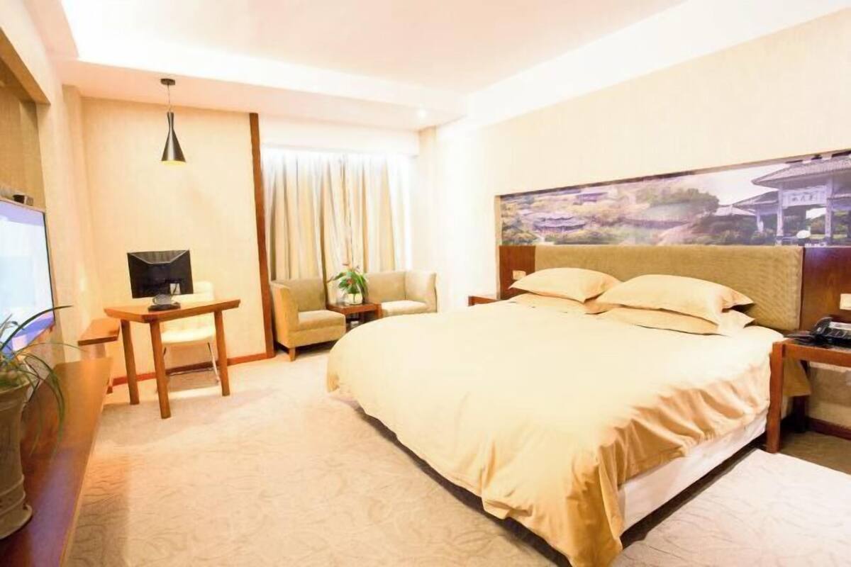 A hotel room with a bed, a desk, a chair, a TV, and a painting on the wall.