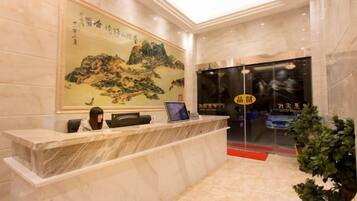 A reception desk with a receptionist, a framed painting, and a glass door entrance.