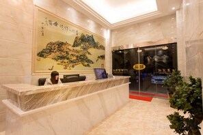 A reception desk with a receptionist, a framed painting, and a glass door entrance. - Zhoushan Shenjiamen Zhongjing Hotel(Banshengdong Passenger Terminal Branch) (Zhoushan)