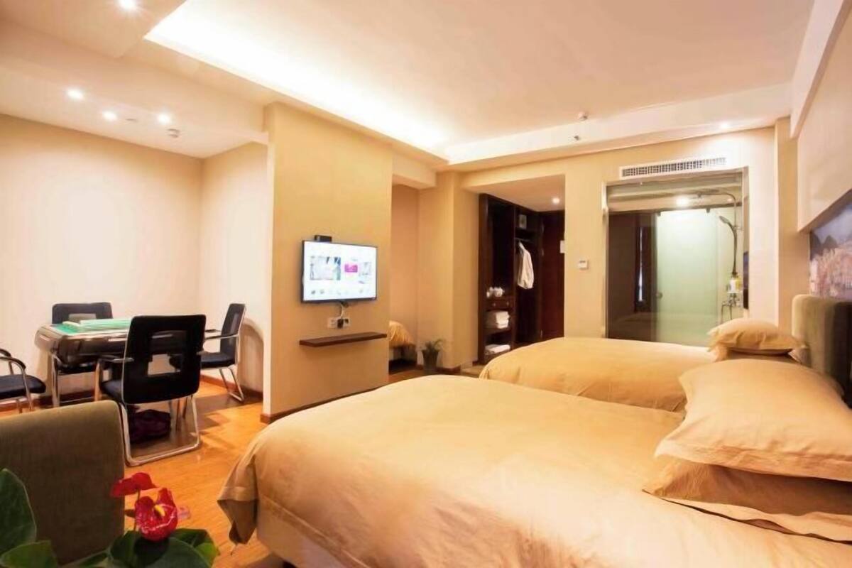 A hotel room with two beds, a desk with a computer, a TV, and a shower area.